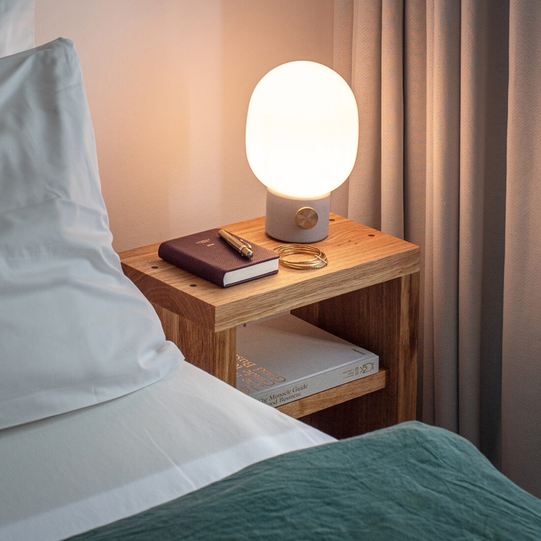 Nachttisch Waldkraft aus Eiche am Bett bei eingeschalteter Nachttischlampe, Notizbuch und Stift auf der Platte